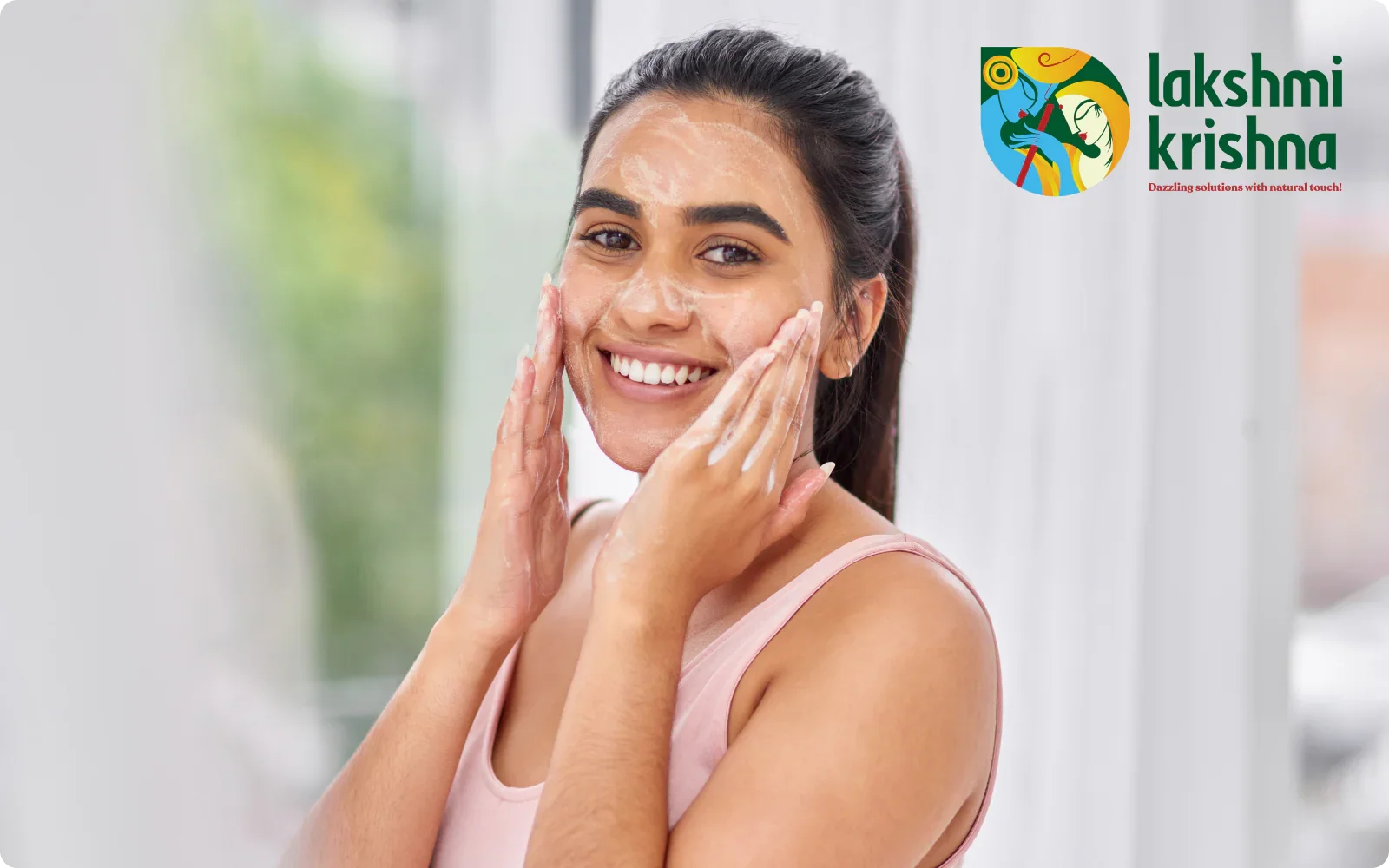 Smiling woman applying foamy face wash cleanser in a bright room with Lakshmi Krishna logo