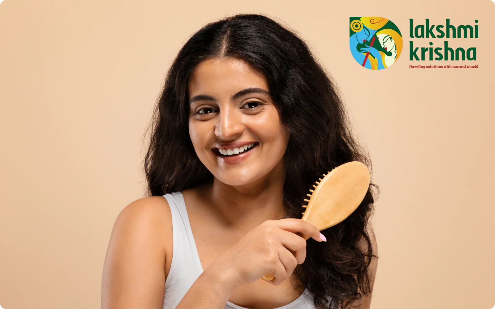 Smiling woman with long dark hair holding a wooden hairbrush against beige background with Lakshmi Krishna logo